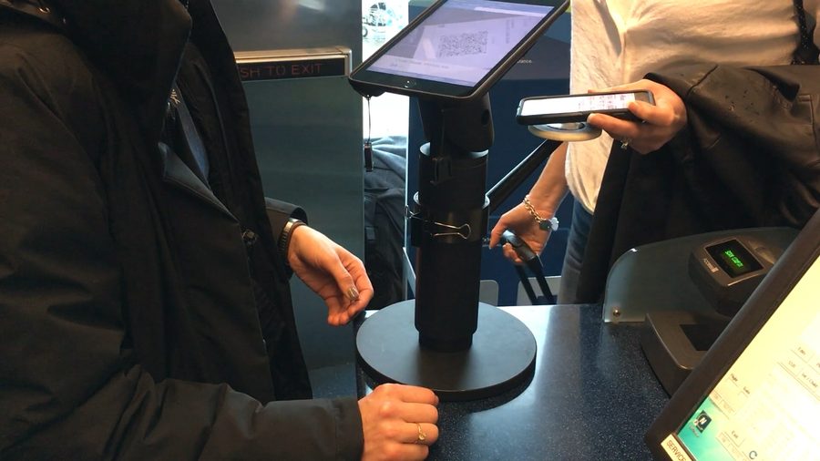 A passenger holds a phone over the boarding pass target on the iPad stand.