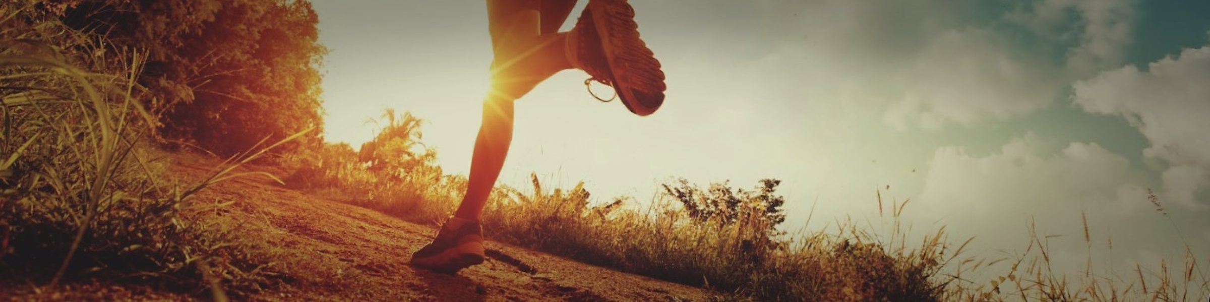 A runner’s legs mid-stride on a trail at sunrise, seen from behind.