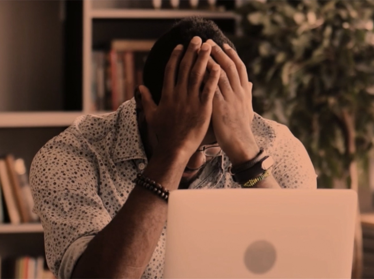 A customer sits at a laptop with their head in their hands, frustrated.